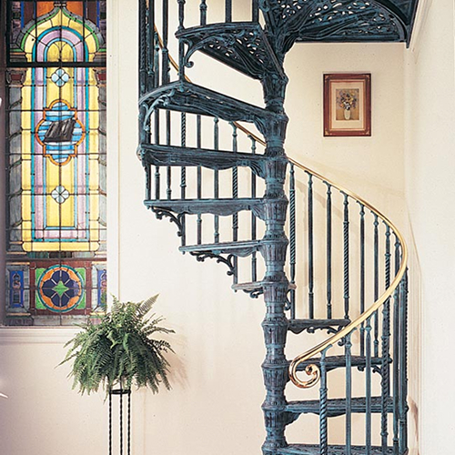 Ornate indoor spiral staircase with decorative scrollwork near a stained glass window