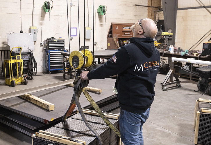 Technician securing steel stock with ratchet straps for staging and shipment at the Iron Shop facility