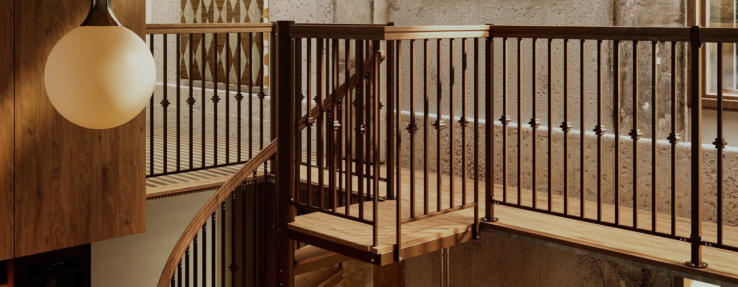 Indoor spiral staircase landing with wood handrail and metal spindle railing along an open loft