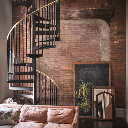 Indoor spiral staircase in a black finish against an exposed brick wall in an urban loft