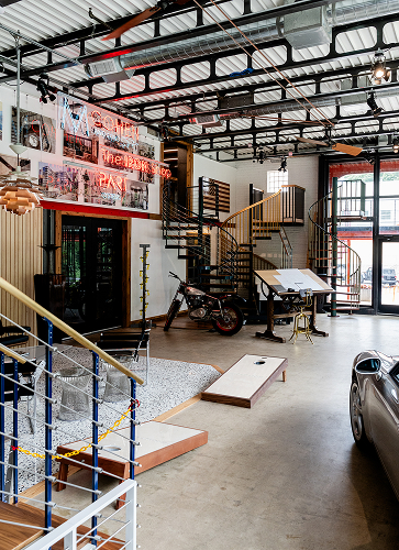 Interior of the Iron Shop facility showing three spiral staircases, neon signage, a vintage motorcycle, and a drafting table in an open showroom space