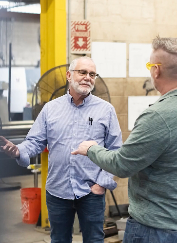 Allen Cohen speaking with a team member on the Iron Shop production floor
