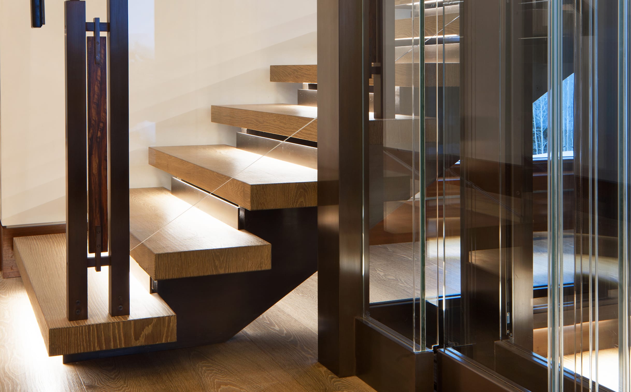 Close-up of a floating wood staircase with glass railing panels and a dark wood post