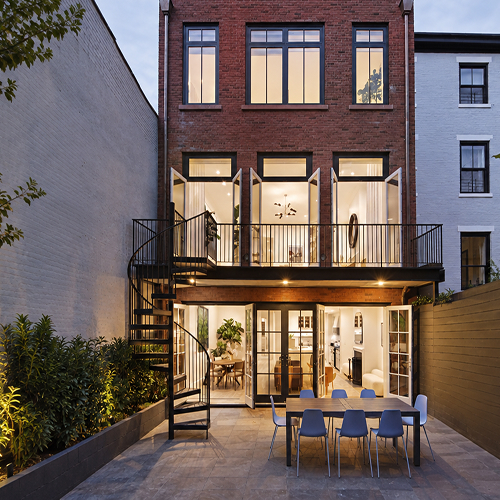 Outdoor spiral staircase in a black finish connecting a balcony to a brick rowhouse backyard patio