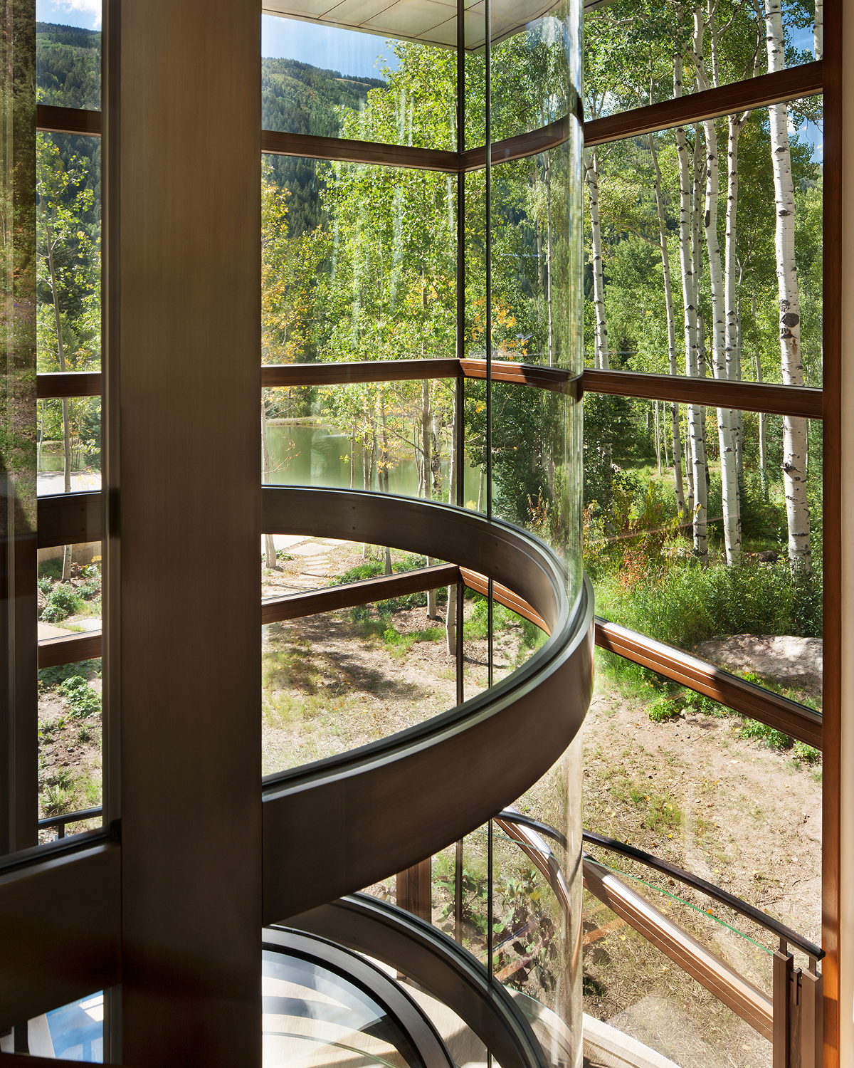Close view from beside a curved glass elevator shaft, looking out through floor-to-ceiling glass panels