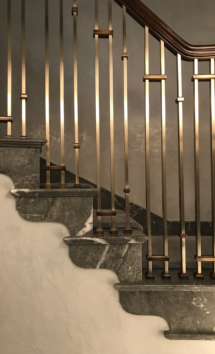 Custom bronze stair railing with square collar spindles and carved stone treads