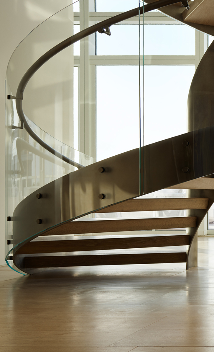 Custom curved floating staircase with glass railing and wood treads cantilevered from a metal stringer, set against floor-to-ceiling windows
