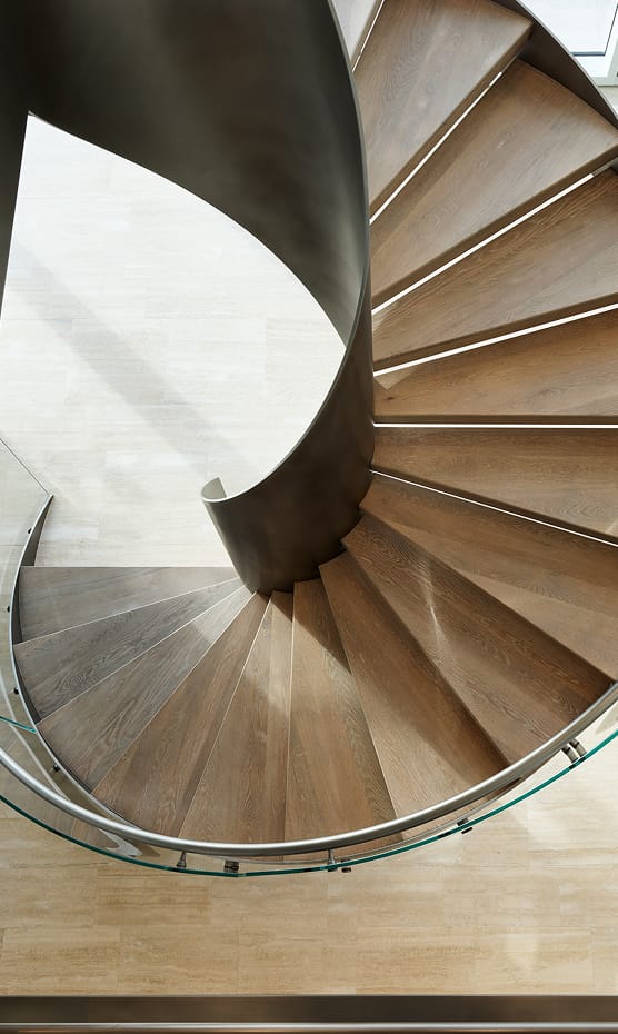 Bird's-eye view of a curved staircase with wood treads, dark steel stringer, and glass railing
