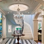 Close view of a curved staircase's scrolled iron railing and marble treads, framed against pale blue walls and a black-and-white diamond marble floor