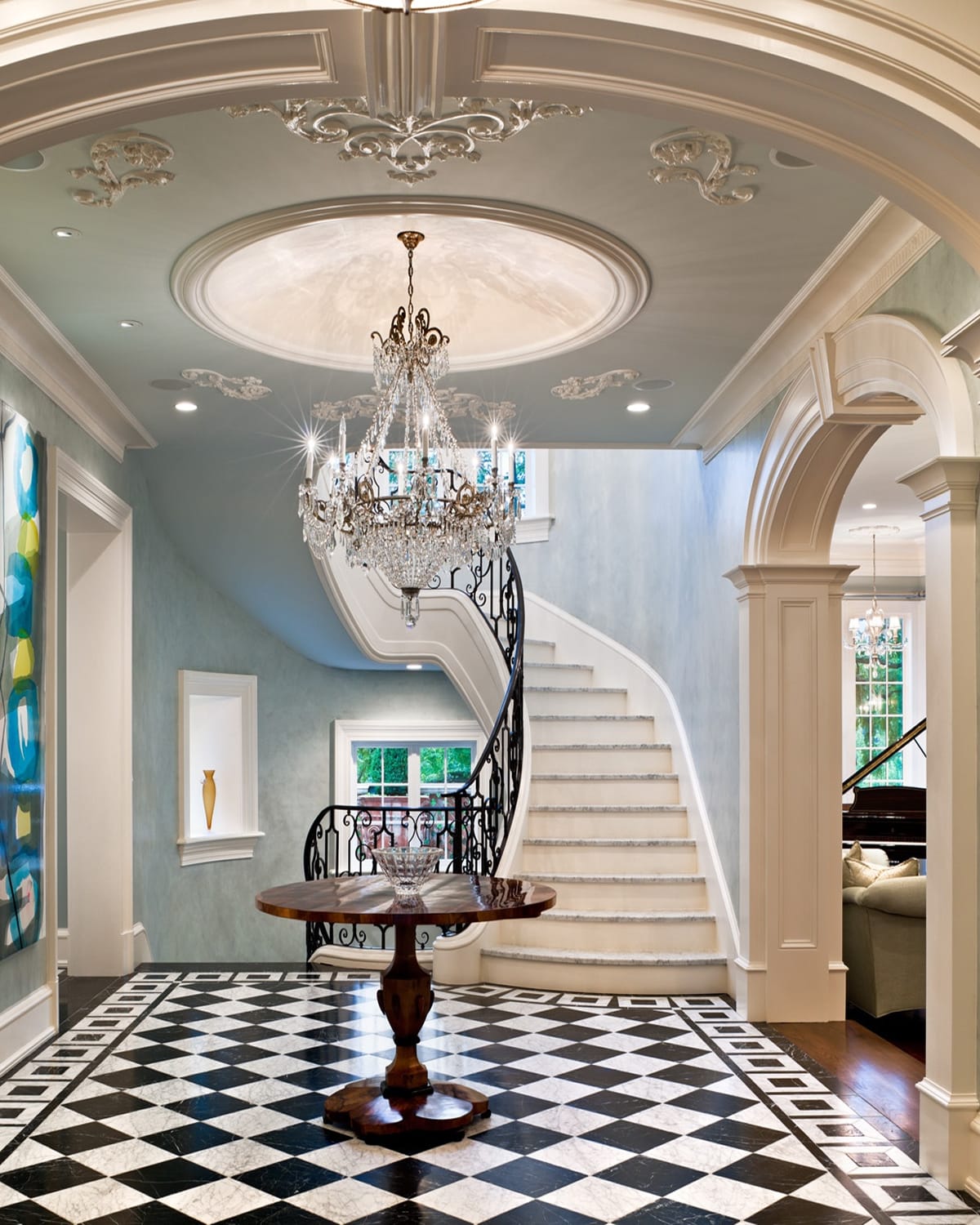Close view of a curved staircase's scrolled iron railing and marble treads, framed against pale blue walls and a black-and-white diamond marble floor