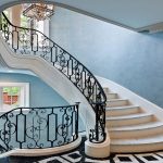 Curved staircase with scrolled iron railing in a Gladwyne, PA entry foyer, with a round wood pedestal table, abstract wall art, and checkered marble flooring