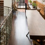 Close detail of a metal stair railing cast in an organic, cell-like lattice pattern, paired with a dark wood handrail and wood treads lit by natural light.