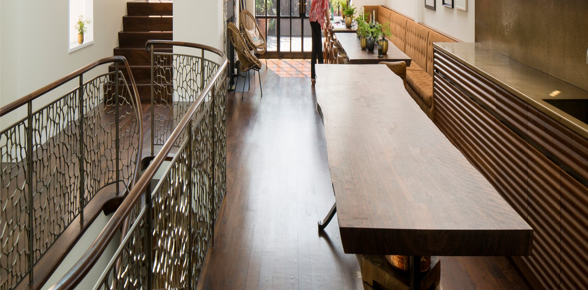 Close detail of a metal stair railing cast in an organic, cell-like lattice pattern, paired with a dark wood handrail and wood treads lit by natural light.