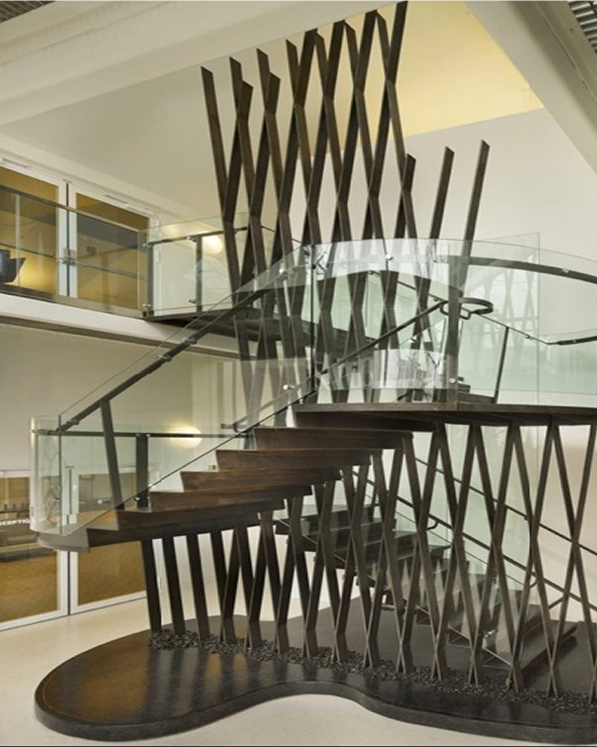 Close view of a sculptural crisscrossed metal installation enclosing a dark wood floating staircase with glass railings