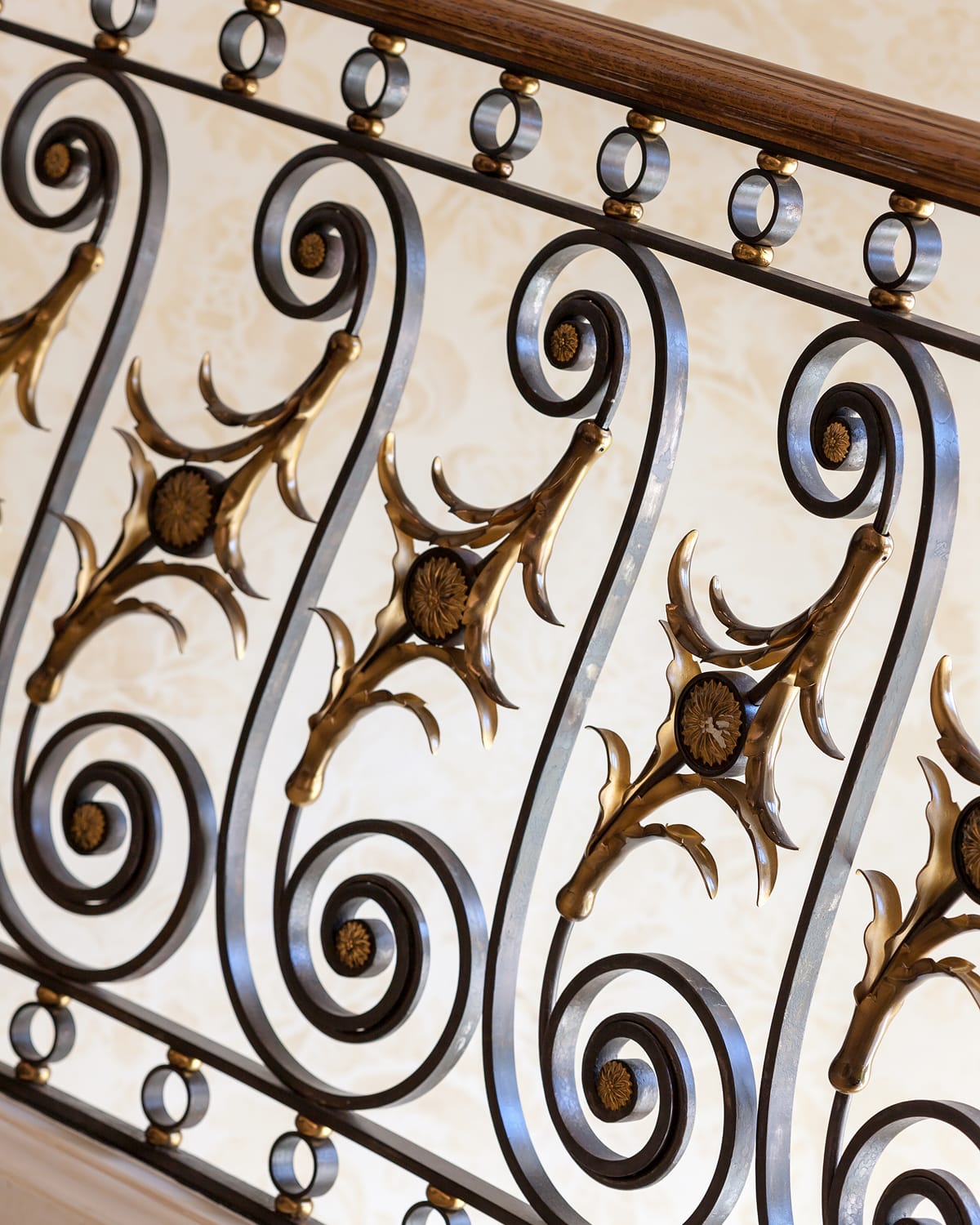 Close detail of a scrolled iron railing panel with gilt-bronze acanthus and rosette accents, set against patterned wallpaper