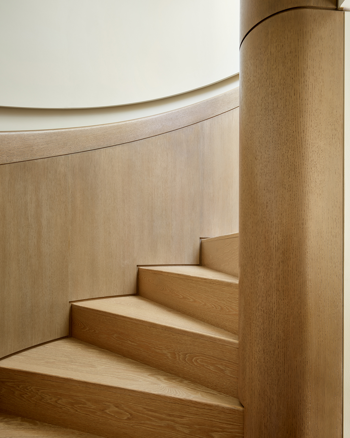 Close detail of light wood stair treads meeting a curved wood-paneled wall and round newel post