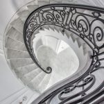 Overhead view of a spiral staircase, showing the full helical run of marble treads and scrolled iron railing coiling down to the base