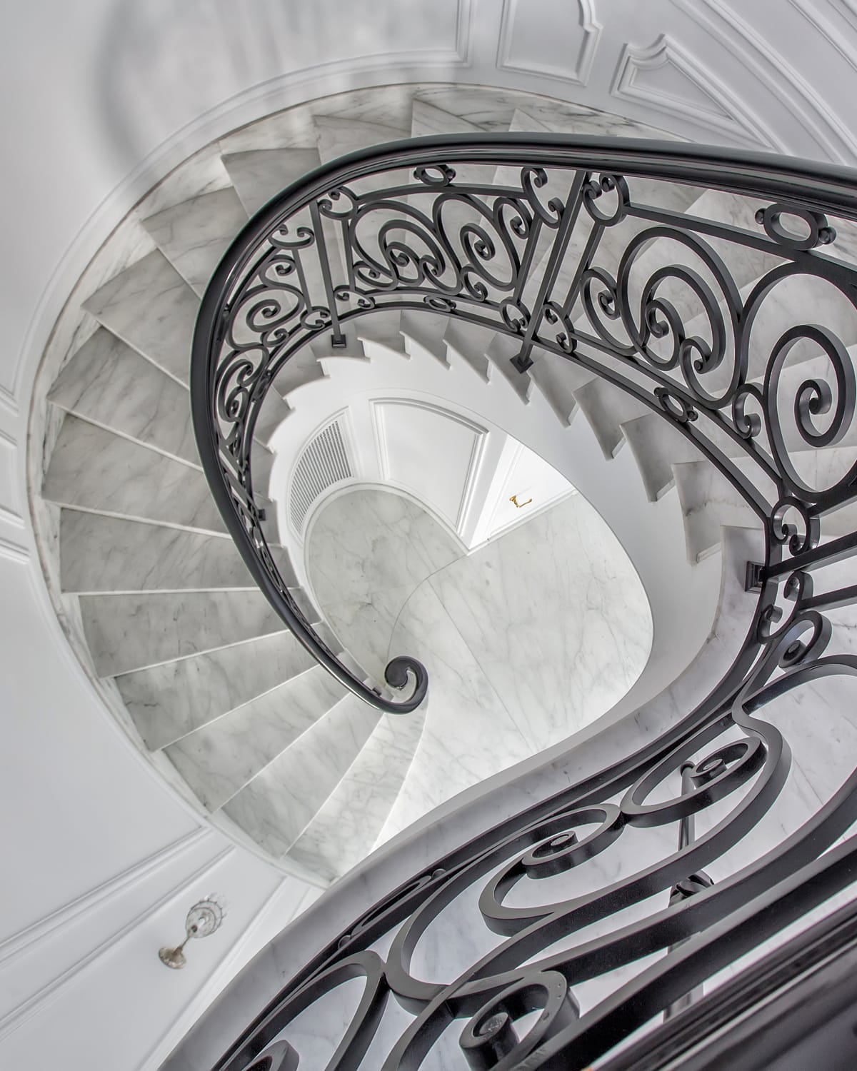 Overhead view of a spiral staircase, showing the full helical run of marble treads and scrolled iron railing coiling down to the base