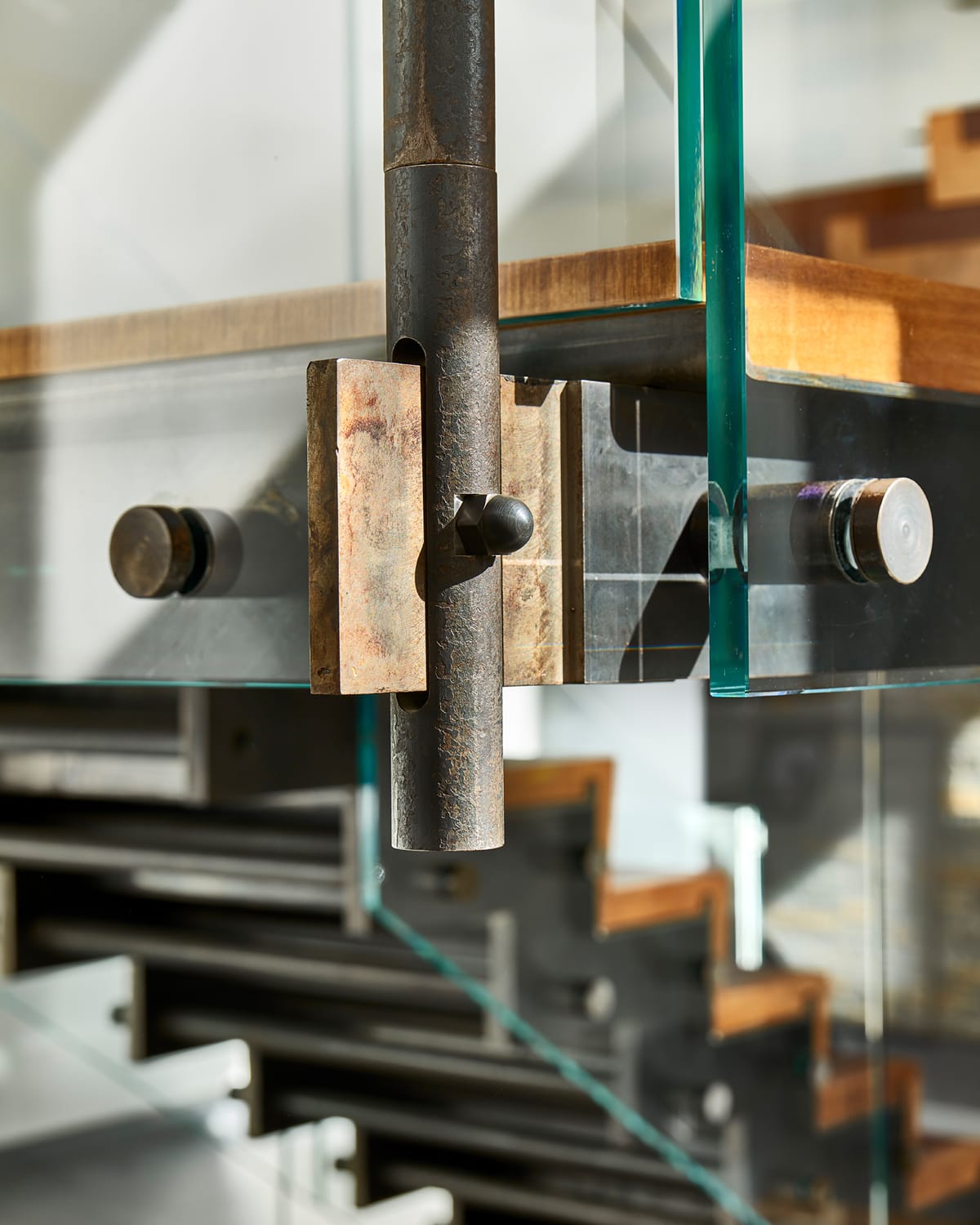 Close detail of a steel bracket and bolt connection joining a glass railing panel to a floating staircase's steel support