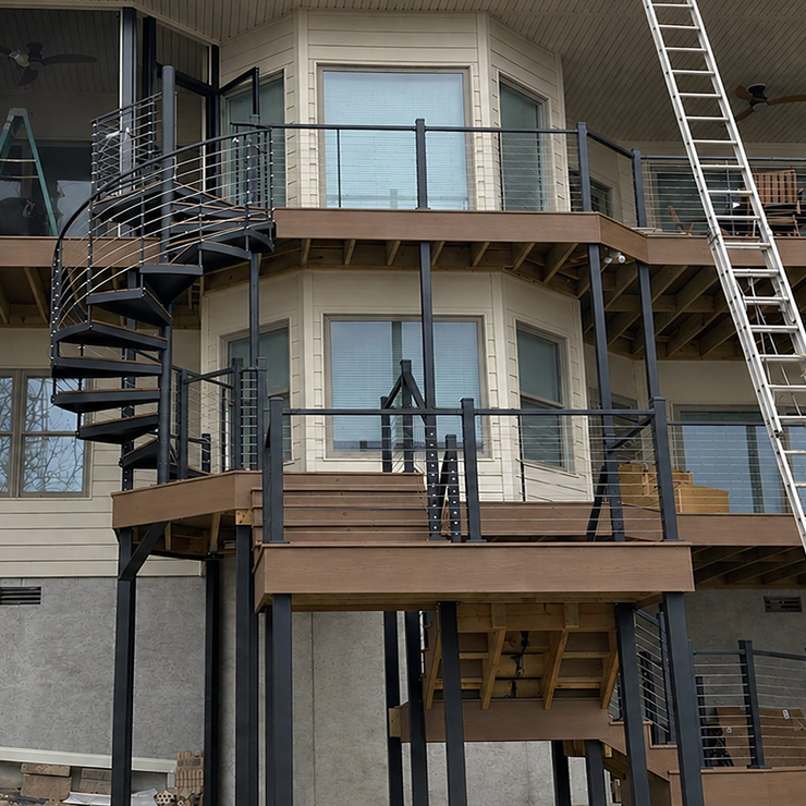 Outdoor spiral staircase connecting multi-level decks on a home under construction, with ladders and exposed framing