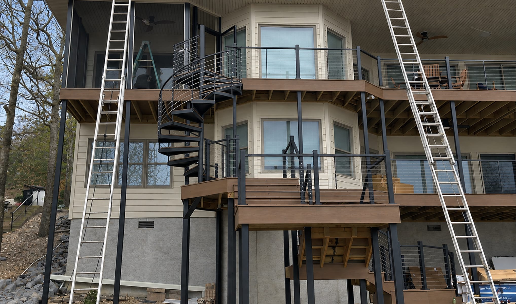 Outdoor spiral staircase connecting multi-level decks on a home under construction, with ladders and exposed framing